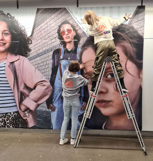 Zu sehen ist ein Sujet, bei dem zwei Werbetechniker ein Werbesujet anbringen