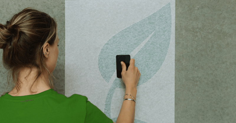Une femme avec T-shirt vert applique un visuel de feuille verte sur un mur, grâce à un tape d'application papier RTape Conform.