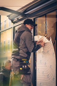 Zu sehen ist ein Folierer, der gerade eine Folie für eine Schaufensterbeklebung anbringt
