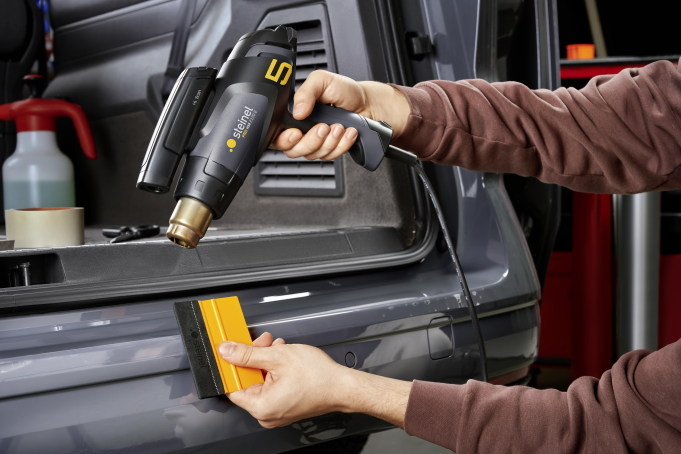 Zu sehen ist ein Car Wrapper, der mit einer Heißluftpistole und Infrarotscanner tempert